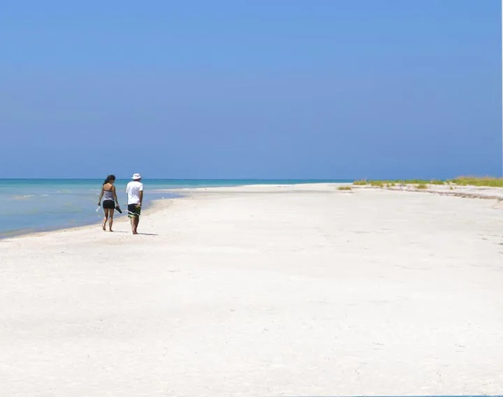 People walking along a Gulf Coast beach at sunset